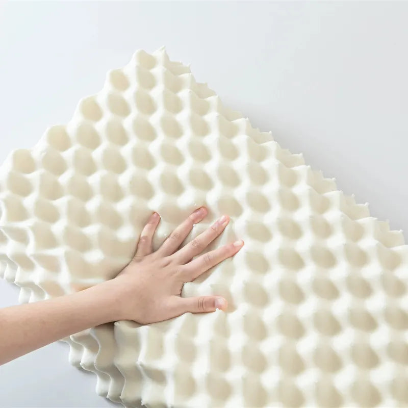 Main appuyée sur la surface en relief d’un oreiller ergonomique en latex naturel format massage, montrant la souplesse et la texture du matériau