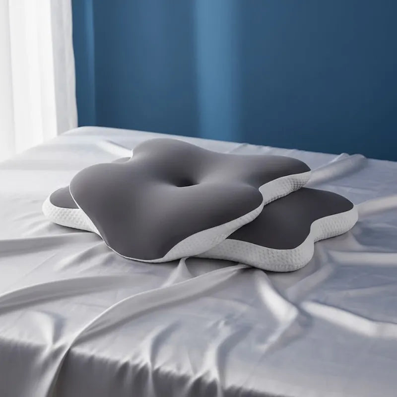 Oreiller memoire de forme douleur cervicale gris fonce sur un drap satiné gris perle devant un mur bleu foncé lumineux