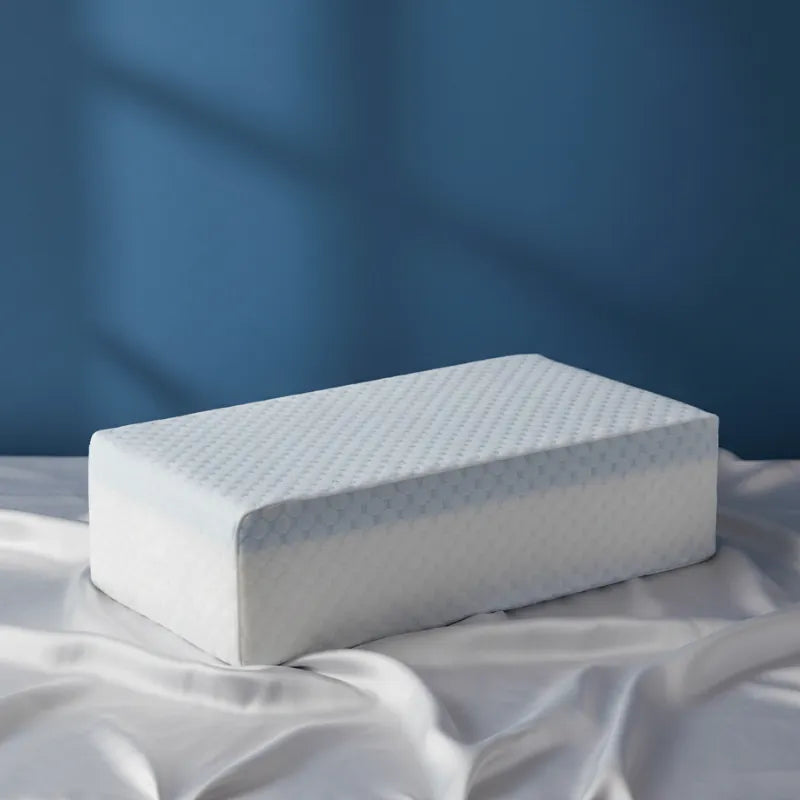 Oreiller mémoire de forme gel rafraichissant 60x30cm posé sur drap satiné gris perle, mur bleu profond, texture alvéolée blanche avec liseré bleu clair