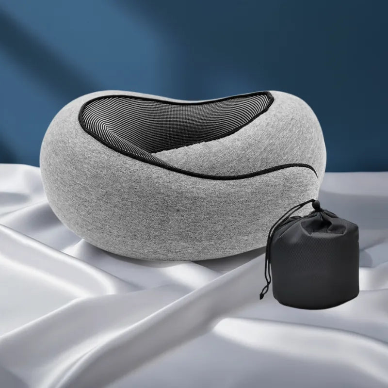 Oreiller mémoire de forme voyage gris avec housse et sac positionné derrière sur fond bleu profond et drap satiné gris perle, style premium