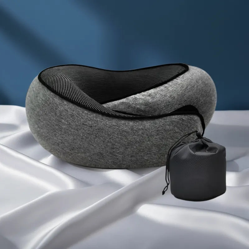 Oreiller mémoire de forme voyage gris foncé avec housse et sac discret à l’arrière sur fond bleu profond et drap satiné gris perle, rendu haut de gamme