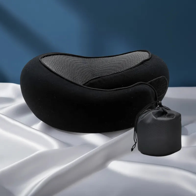 Oreiller mémoire de forme voyage noir avec housse et sac placé en retrait derrière sur fond bleu profond et drap satiné gris perle, style réaliste premium