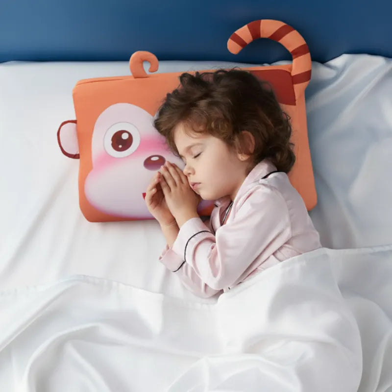 Enfant endormi paisiblement sur un oreiller mémoire de forme enfant singe dans une ambiance douce et premium.