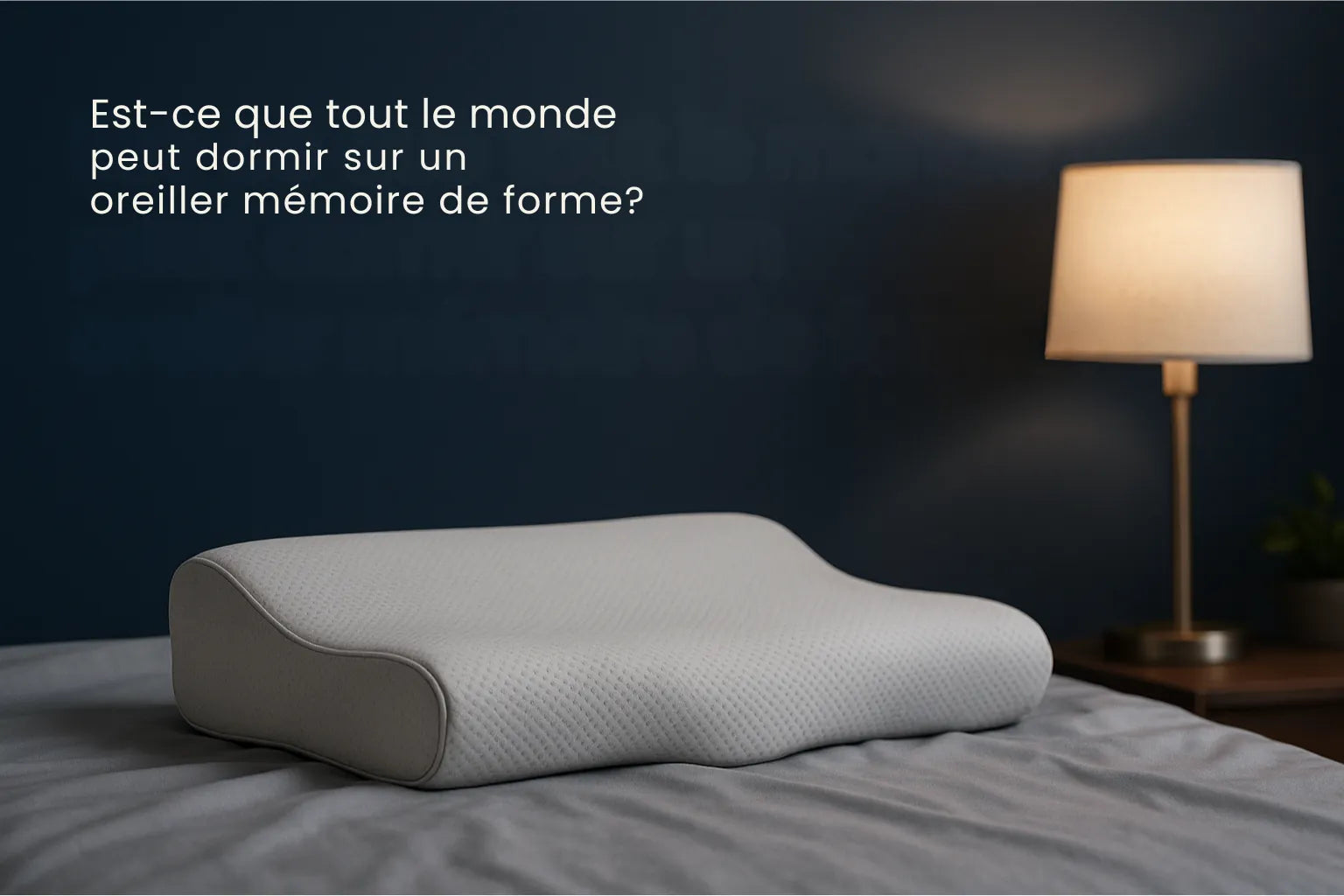 Oreiller ergonomique à mémoire de forme posé sur un lit aux draps gris perle, éclairé par une lampe de chevet devant un mur bleu profond, avec le titre Est-ce que tout le monde peut dormir sur un oreiller mémoire de forme