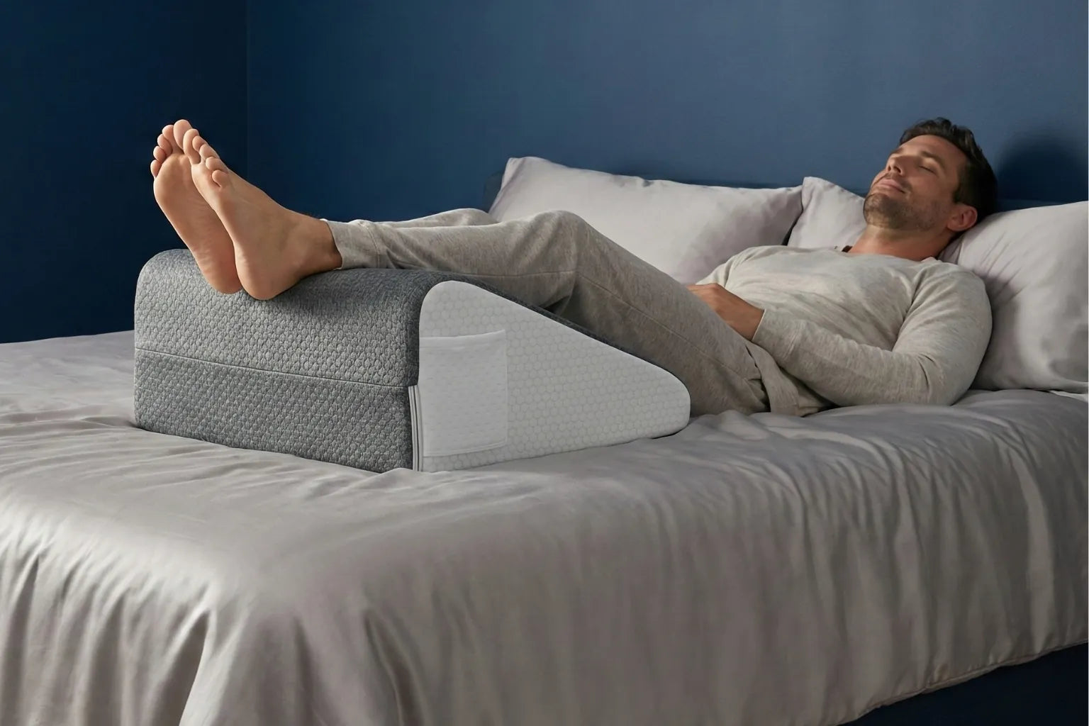 Coussin ergonomique placé sous les jambes pour soulager les jambes lourdes, en position allongée sur un lit, dans un contexte de repos et de confort nocturne