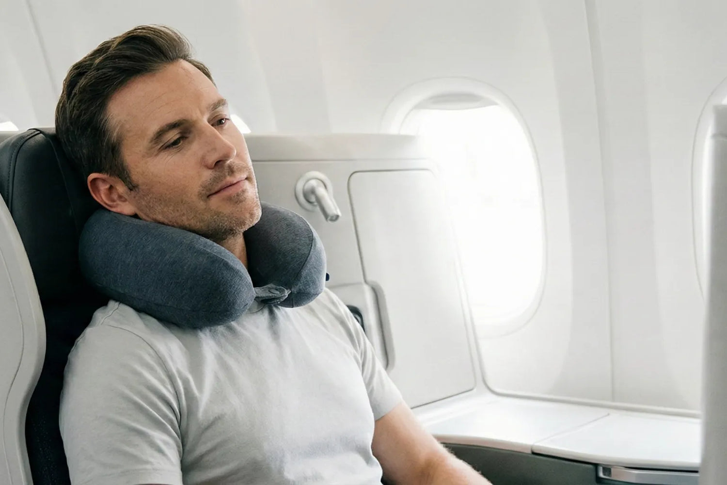 Homme assis dans un avion portant un oreiller de voyage autour du cou, en position de repos naturelle pendant un vol
