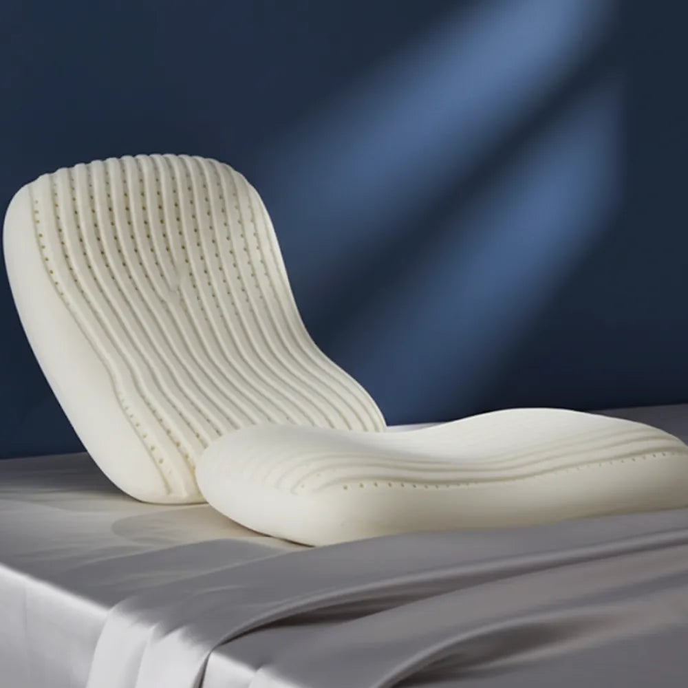 Oreiller ergonomique en latex — modèle rainuré blanc conçu pour un bon soutien de la nuque et de la tête, présenté sur un drap satiné gris perle devant un mur bleu profond.