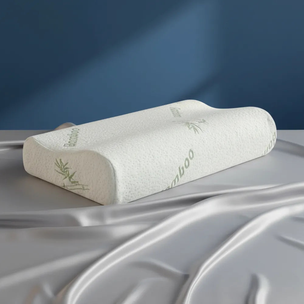Oreiller ergonomique en mémoire de forme bambou — modèle cervical blanc avec housse respirante en fibre de bambou, présenté sur un drap satiné gris perle devant un mur bleu profond.