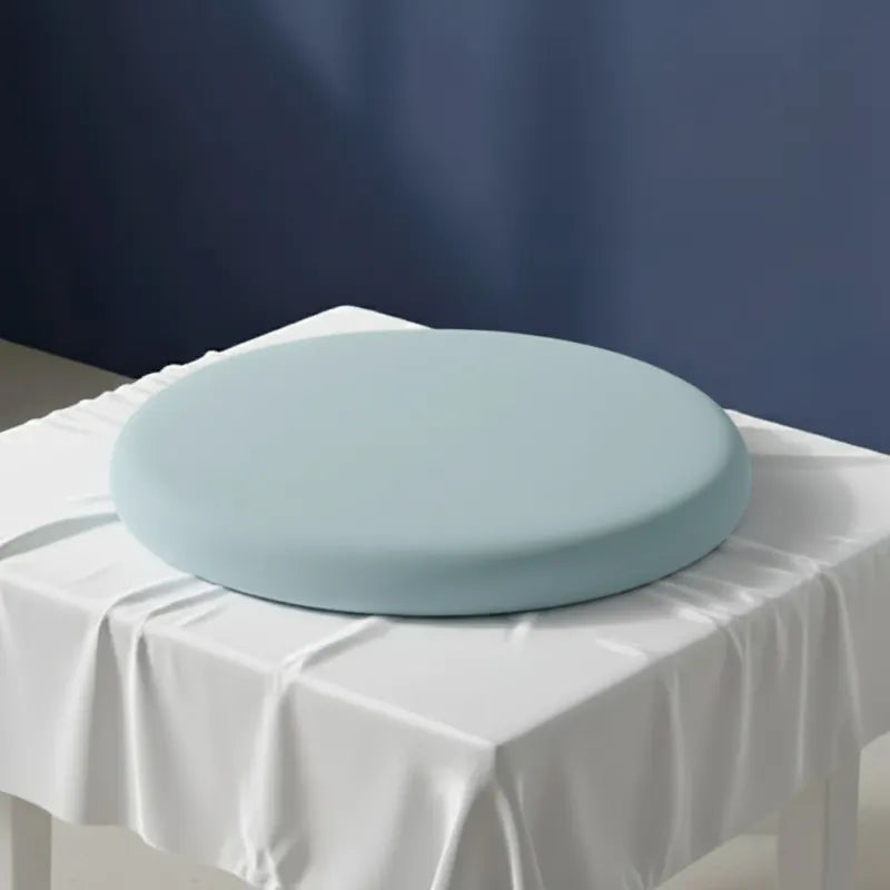 Coussin ergonomique rond bleu ciel pour chaise de bureau, en mousse mémoire de forme, sur un drap satiné gris perle et fond bleu.