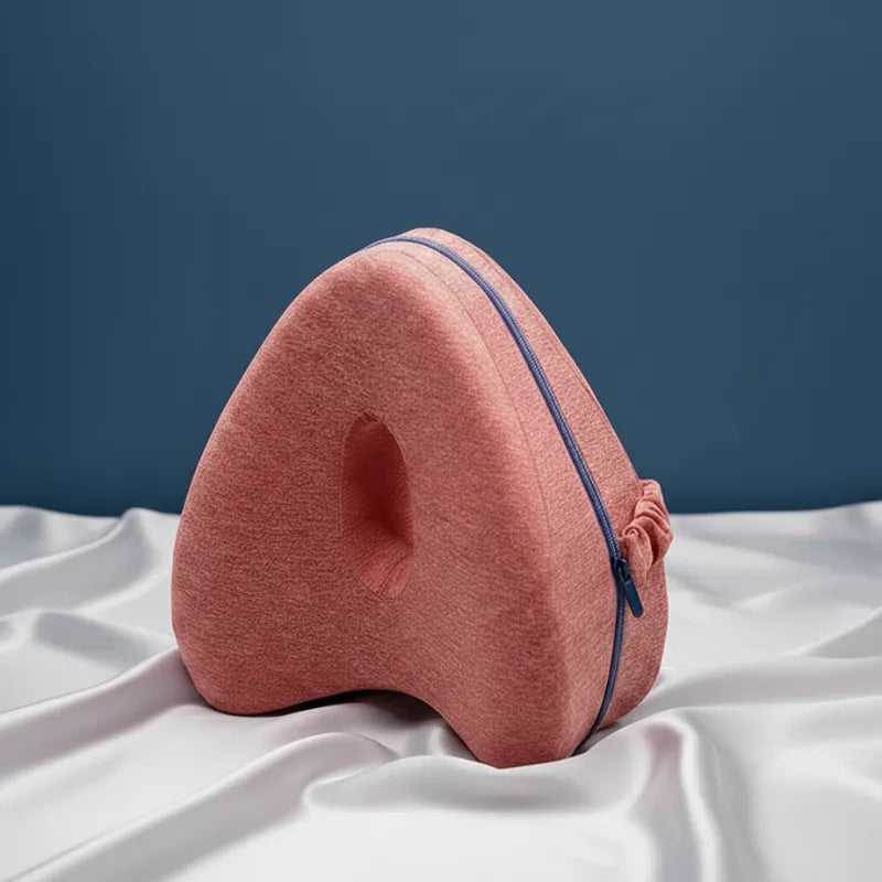 Coussin ergonomique entre les jambes rouge posé sur drap gris perle avec fond bleu uni et éclairage naturel