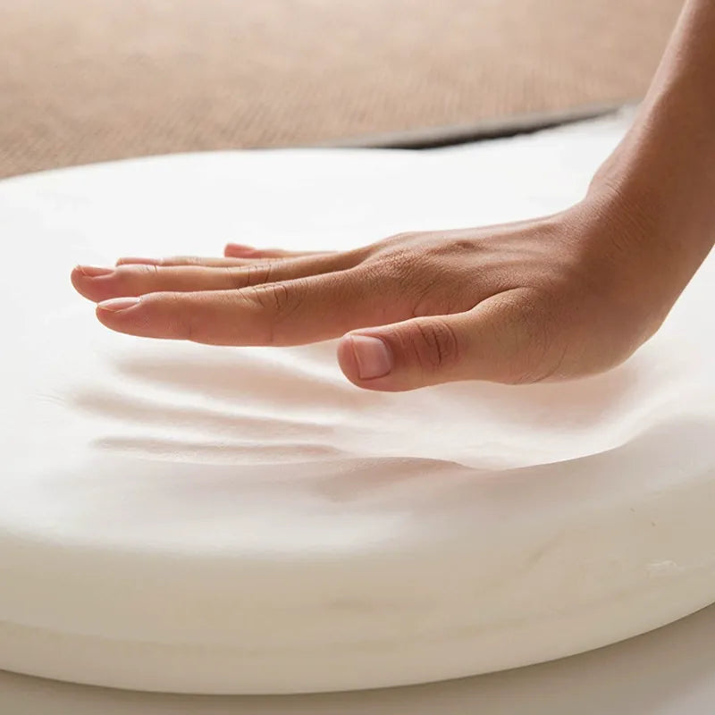 Main pressant la mousse à mémoire de forme du coussin ergonomique rond bleu ciel, démonstration du confort et de la répartition des pressions.