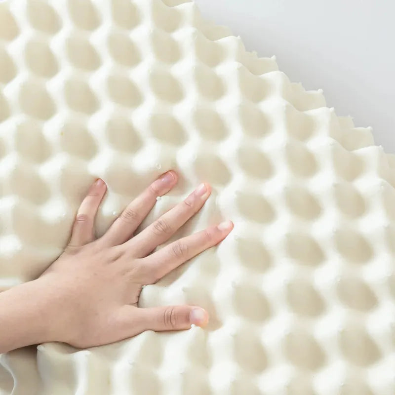 Gros plan sur un oreiller ergonomique compact en latex naturel, avec une main pressant les reliefs pour illustrer la flexibilité du matériau
