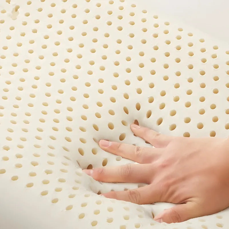 Gros plan sur un oreiller en latex naturel concave, avec une main pressant la zone perforée pour illustrer la flexibilité et la ventilation