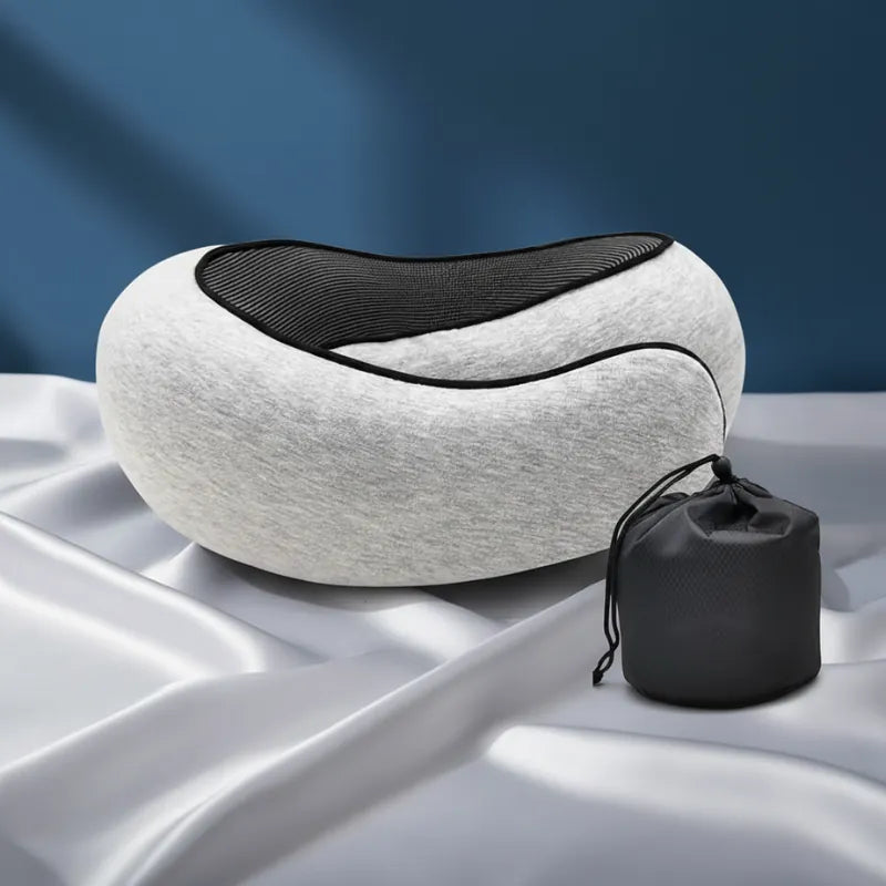 Oreiller mémoire de forme voyage gris clair avec housse et sac légèrement en retrait sur fond bleu profond et drap satiné gris perle, style premium